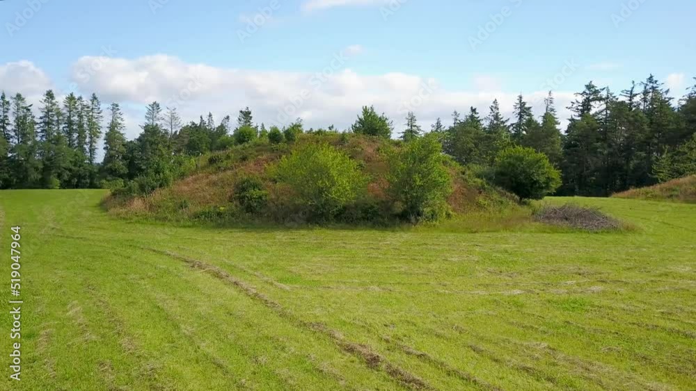 Tumulus, Or Ancient Burial Mound, On Lush Green Field In Denmark On A Sunny Day. aerial orbit Tumulus, Or Ancient Burial Mound, On Lush Green Field In Denmark On A Sunny Day. aerial orbit