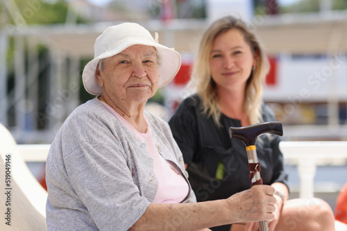 Old granny with cane sitting on bench with young smiling female