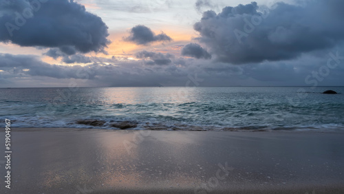 Tropical sunset. The sky between dark blue clouds is highlighted yellow, pink. Reflection on the surface of the ocean and the wet sand of the beach. Seychelles. Mahe. Beau Vallon