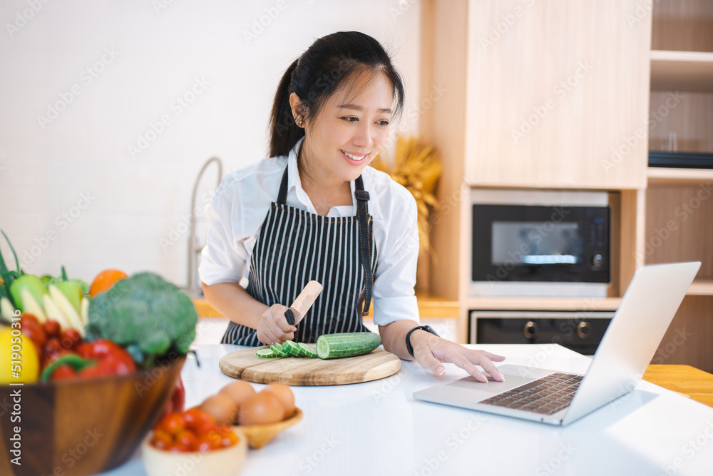 Woman in kitchen following recipe on digital laptop Woman in kitchen following recipe on digital laptop
