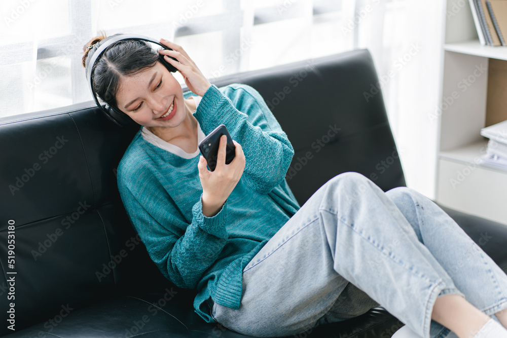 Fototapeta premium smiling girl relaxing at home She is listening to music using her smartphone and wearing headphones.