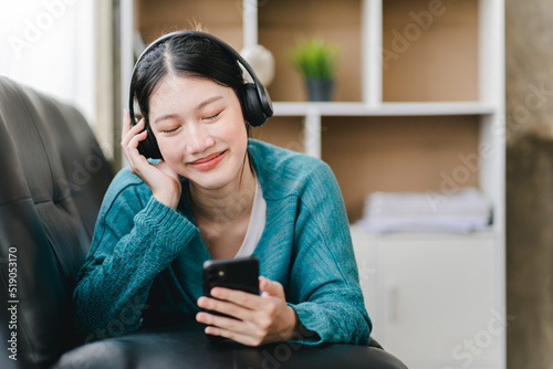 smiling girl relaxing at home She is listening to music using her smartphone and wearing headphones.