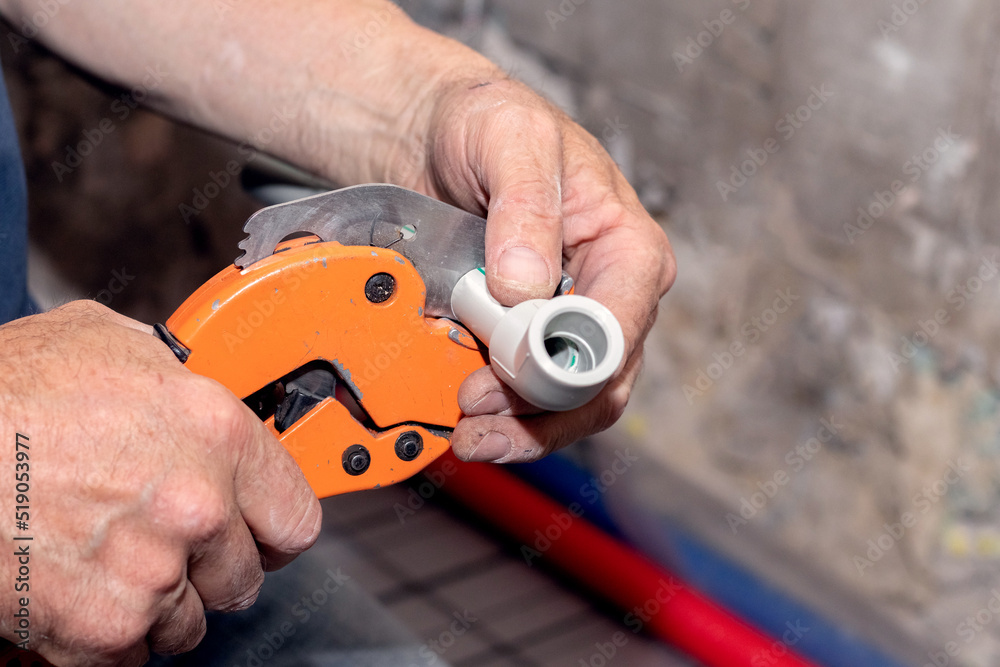 A plumber uses a special scissors to cut a polypropylene pipe during the installation of a water pipe
