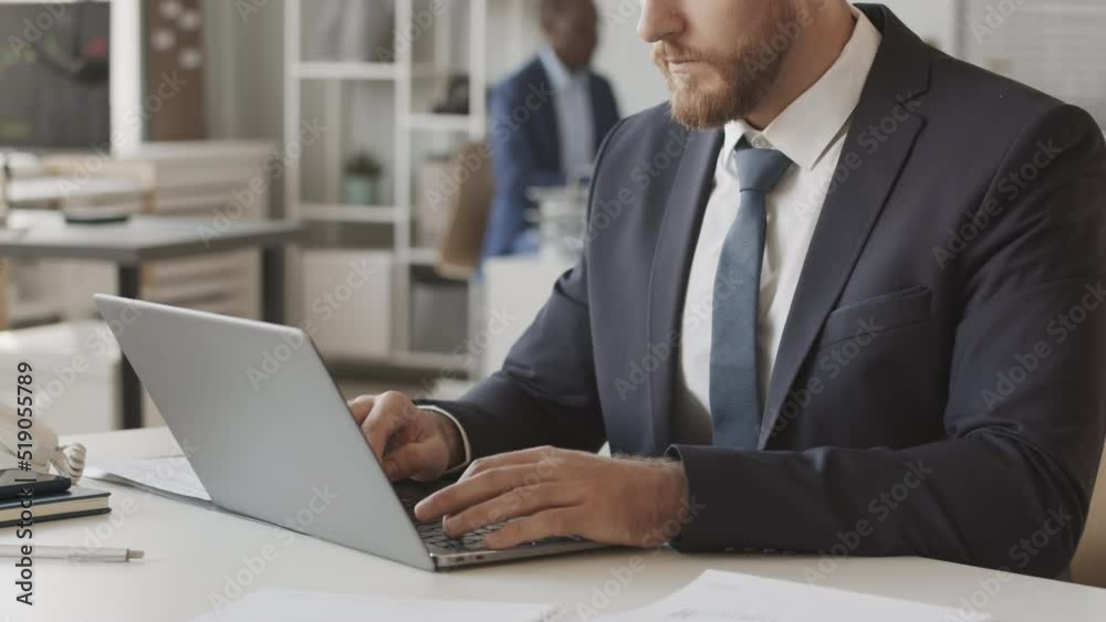 Cropped slowmo of Caucasian male financial analyst in suit typing on laptop, working at stock exchange company with African American colleague sitting in background Cropped slowmo of Caucasian male financial analyst in suit typing on laptop, working at stock exchange company with African American colleague sitting in background