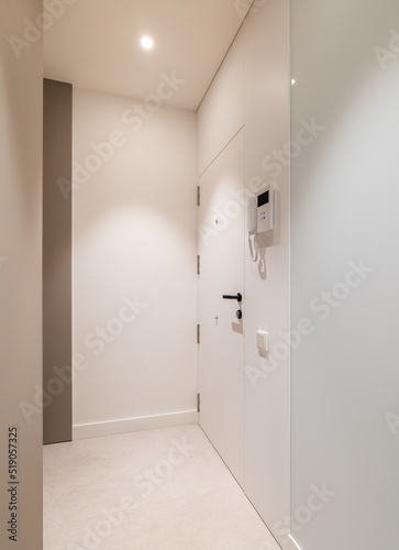 Vertical view of entrance hall area in modern refurbished apartment. White walls and door with intercom system.