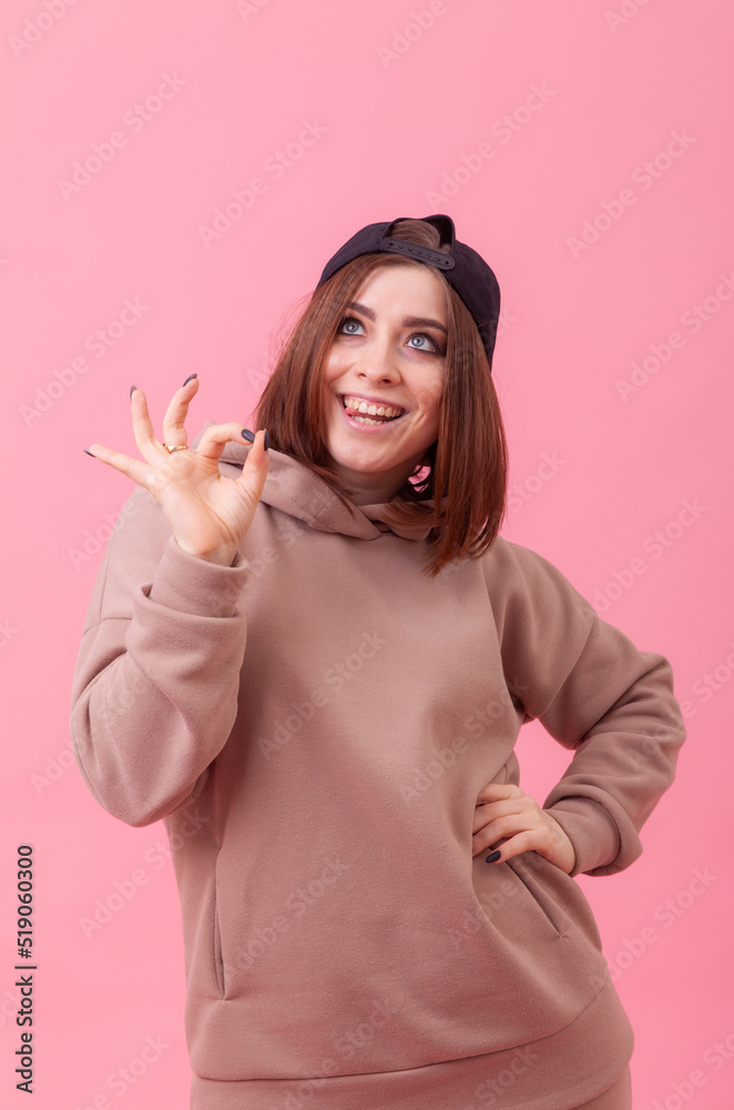 Portrait of an emotionally positive young woman with an inverted cap, wearing a hoodie on a pink background Portrait of an emotionally positive young woman with an inverted cap, wearing a hoodie on a pink background