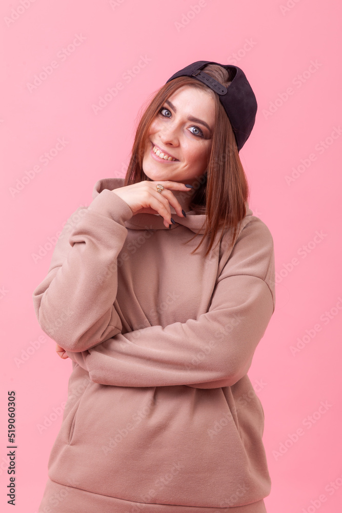 Portrait of an emotionally positive young woman with an inverted cap, wearing a hoodie on a pink background Portrait of an emotionally positive young woman with an inverted cap, wearing a hoodie on a pink background