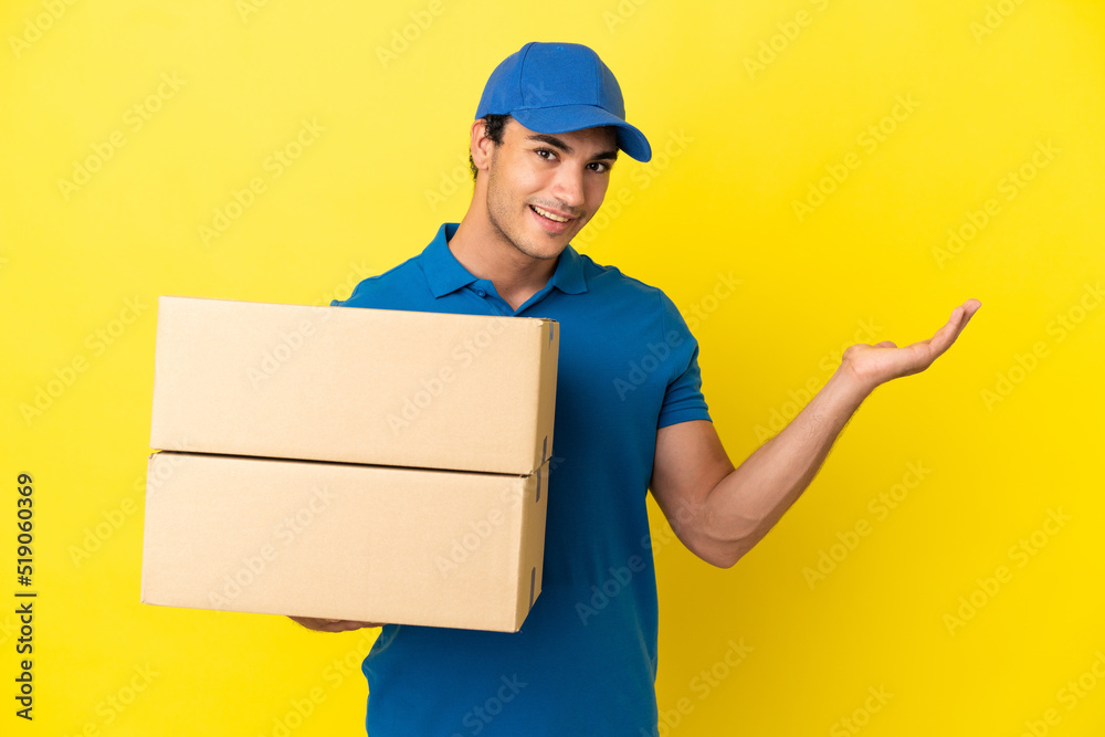 Delivery man over isolated yellow wall extending hands to the side for inviting to come Delivery man over isolated yellow wall extending hands to the side for inviting to come