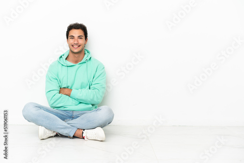 Caucasian handsome man sitting on the floor with arms crossed and looking forward