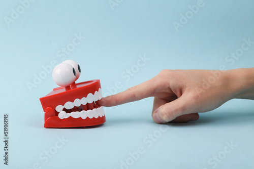 Fotografija Funny toy clockwork jumping teeth with eyes biting finger of hand, blue background