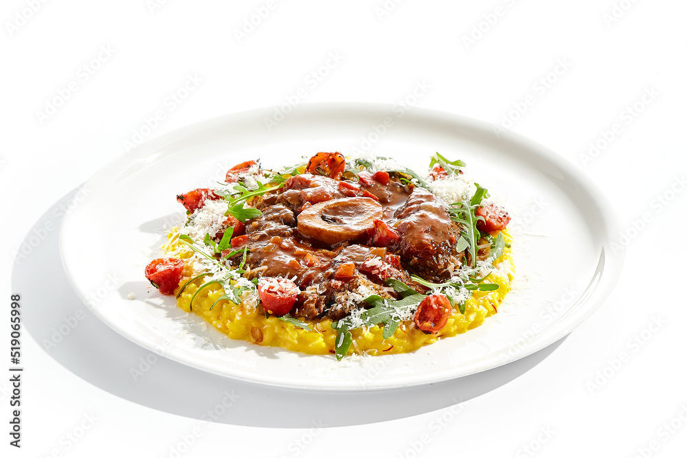 Traditional Italian dish - osso buco with risotto Milanese and cherry tomato and rucola. Ossobuco with saffron rice isolated on white background. Stewed meat on bone with yellow risotto. Traditional Italian dish - osso buco with risotto Milanese and cherry tomato and rucola. Ossobuco with saffron rice isolated on white background. Stewed meat on bone with yellow risotto.