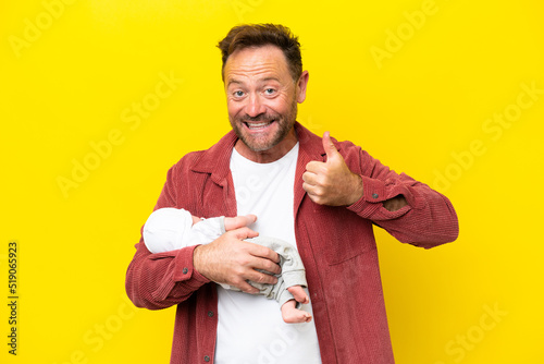 Middle age caucasian man holding his newborn son isolated on yellow background with thumbs up because something good has happened