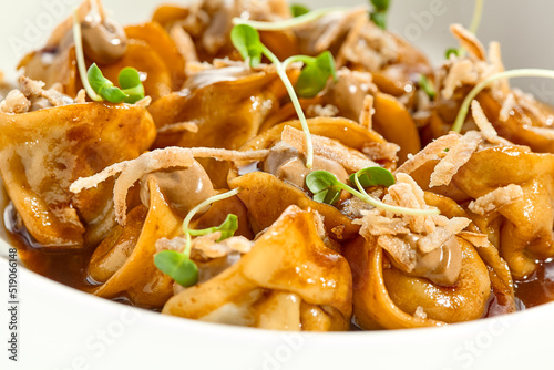 Fototapeta Naklejka Na Ścianę i Meble -  Main course in italian cuisine - meat tortellini with demi-glace sauce and mushroom cream. Beef ravioli on white plate. Tortellini with minced veal in beef sauce. Gourmet cuisine in restaurant menu.