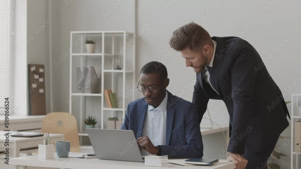 Slowmo of two successful diverse traders in formal suits looking at laptop display and discussing online stock market and cryptocurrency index Slowmo of two successful diverse traders in formal suits looking at laptop display and discussing online stock market and cryptocurrency index