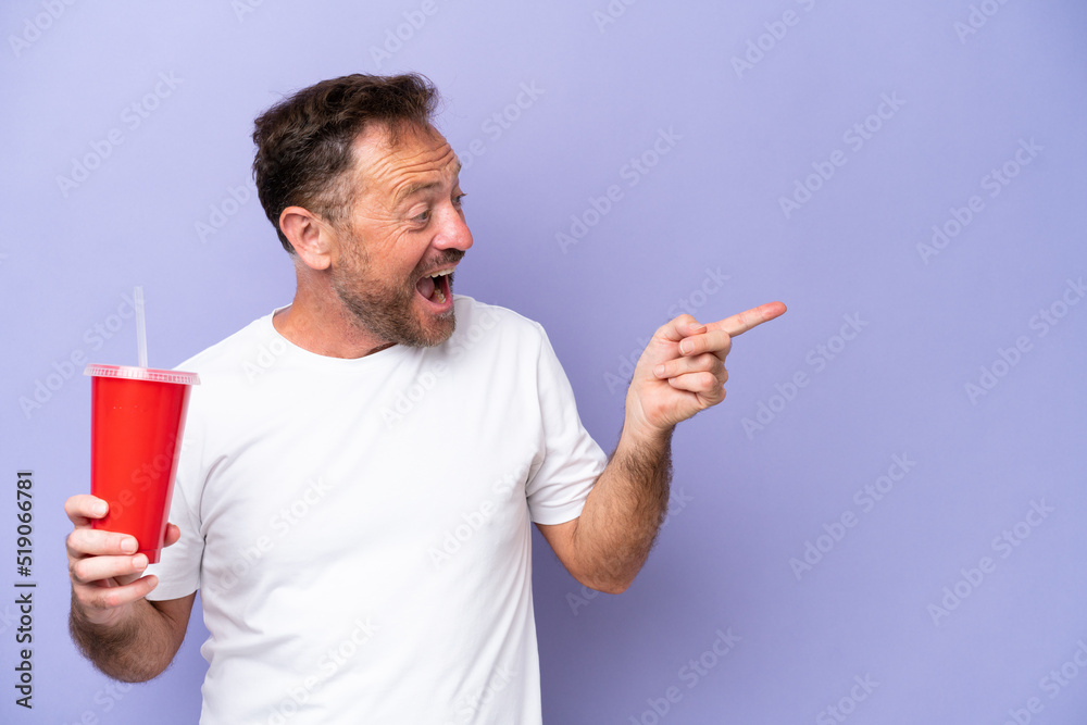 Middle age caucasian man holding soda isolated on purple background pointing finger to the side and presenting a product Middle age caucasian man holding soda isolated on purple background pointing finger to the side and presenting a product