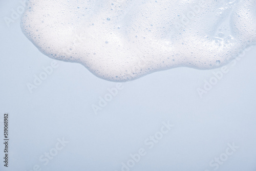 Face cleansing mousse sample. White cleanser foam bubbles on blue background. Soap, shower gel, shampoo foam texture closeup