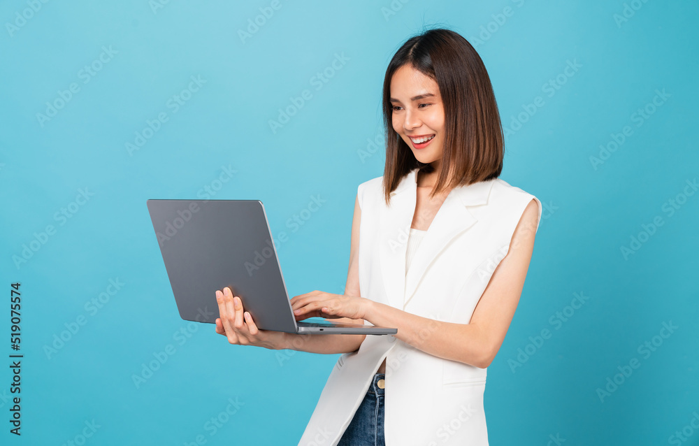 Studio shot of cheerful beautiful Asian woman holding laptop with typing on keyboard on blue background. Studio shot of cheerful beautiful Asian woman holding laptop with typing on keyboard on blue background.