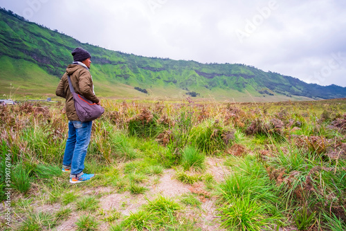 Photo of backside of asian man standing in the middle of meadow in mount bromo on a cloudy morning