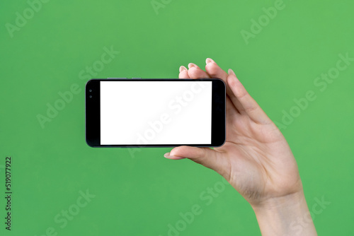 Mobile mockup. Online advertising. Internet technology. Female hand holding smartphone with blank screen isolated green.