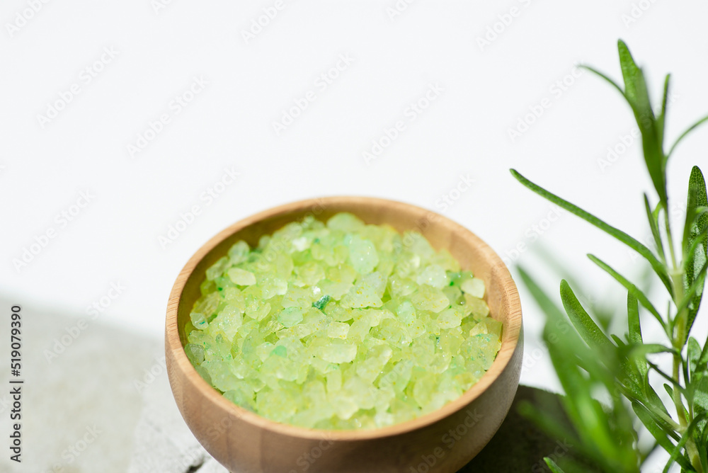 Wooden bowl with green bath sea salt with rosemary branch. Beauty treatment for spa and wellness on grey and white background. Skincare natural cosmetic concept for body care Wooden bowl with green bath sea salt with rosemary branch. Beauty treatment for spa and wellness on grey and white background. Skincare natural cosmetic concept for body care