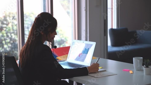Asian Female Customer service is taking telephone call and noting down information on to a paper.