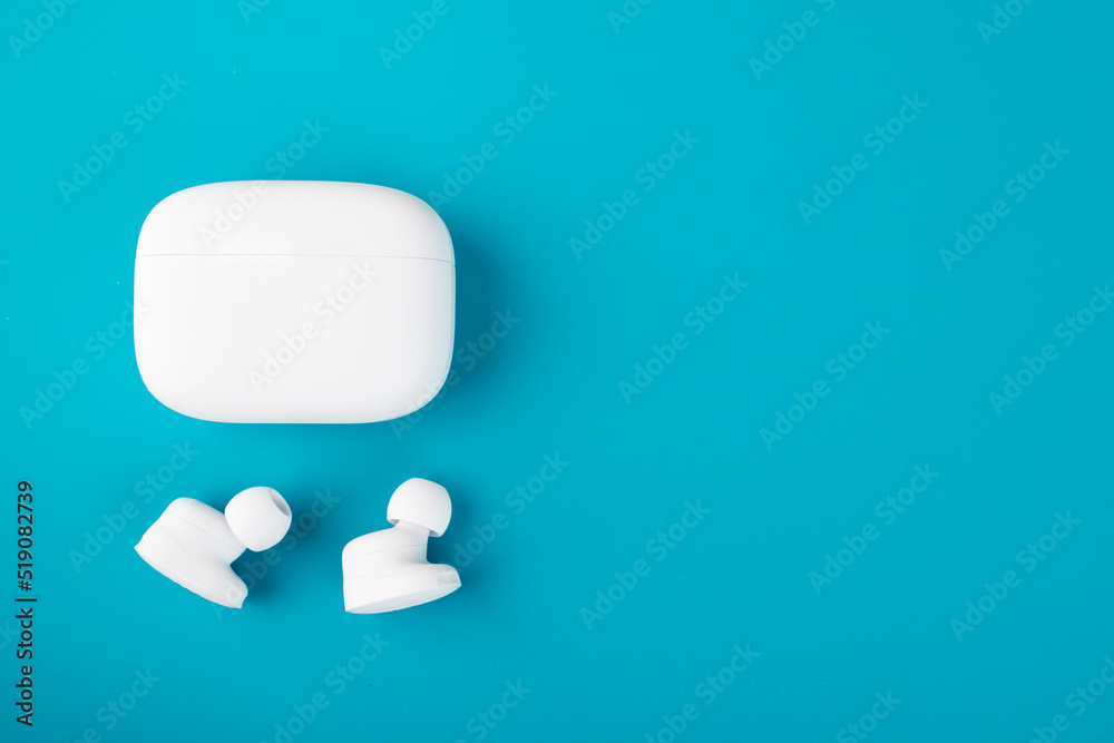 wireless earflaps, small headphones with a charging case on a blue background with copy space wireless earflaps, small headphones with a charging case on a blue background with copy space