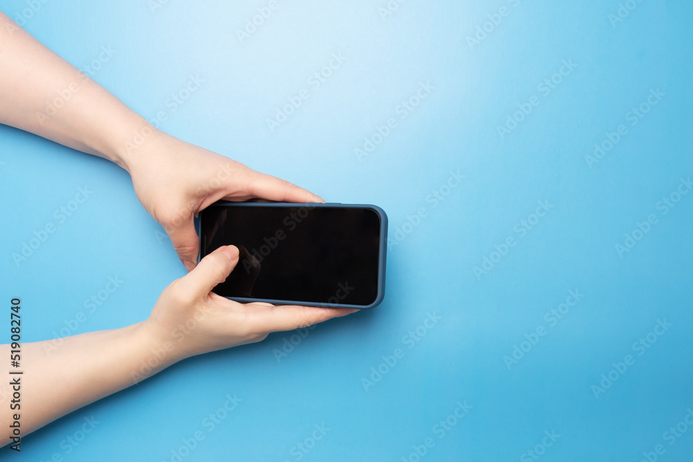 female hand with phone on blue background top view
