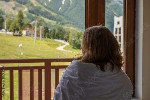woman in the morning at the hotel looks at the mountains from the bed in a blanket