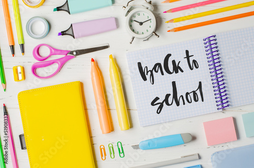 Children's accessories for study, creativity and office supplies on a white wooden background. Handwritten inscription Back to school on a white notebook.