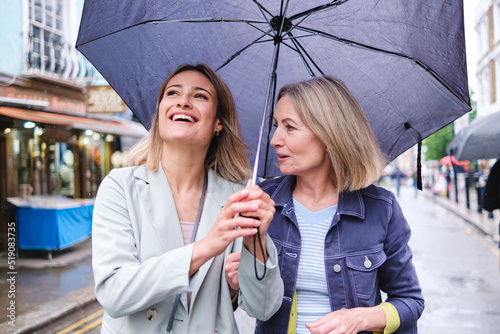 Mother and daughter with umbrella walking together on street photo