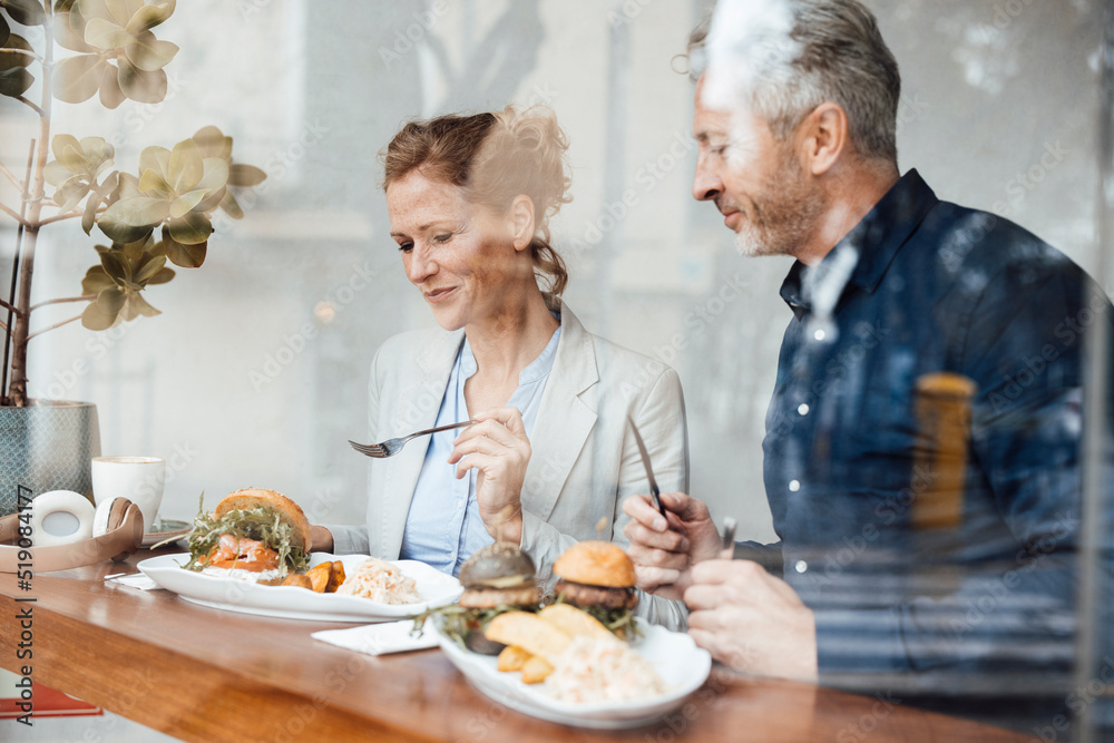 Smiling businesswoman with businessman having lunch in cafe seen through glass Smiling businesswoman with businessman having lunch in cafe seen through glass