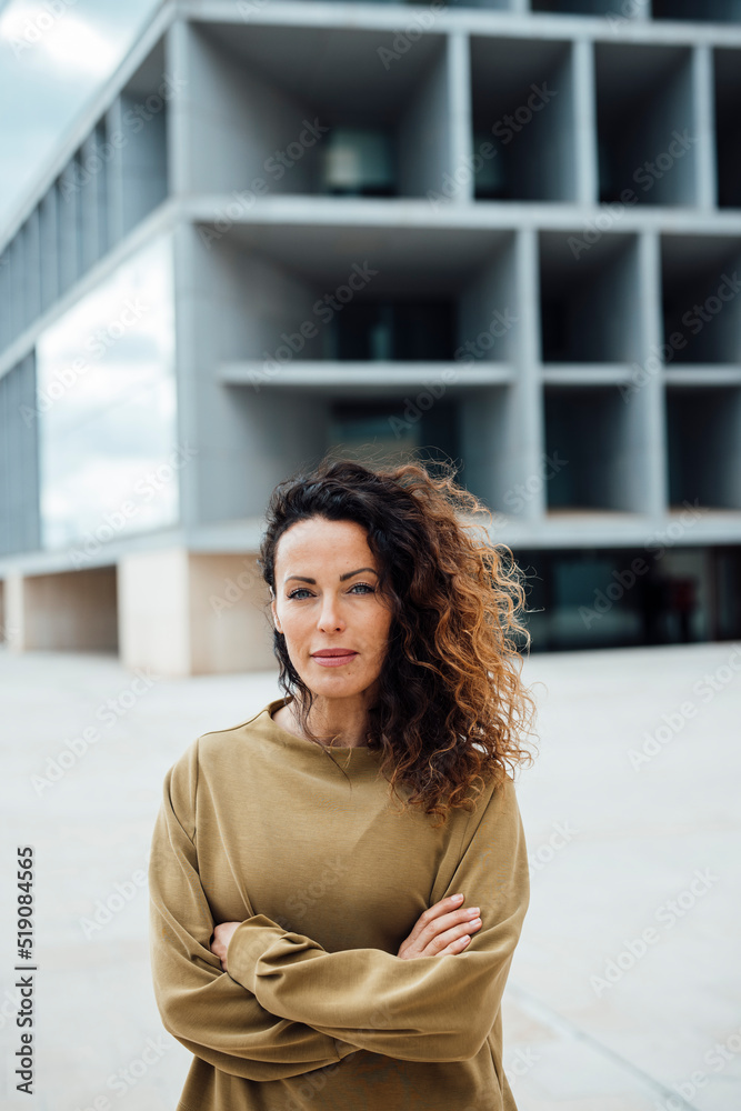 Confident businesswoman with arms crossed standing in front of office building Confident businesswoman with arms crossed standing in front of office building