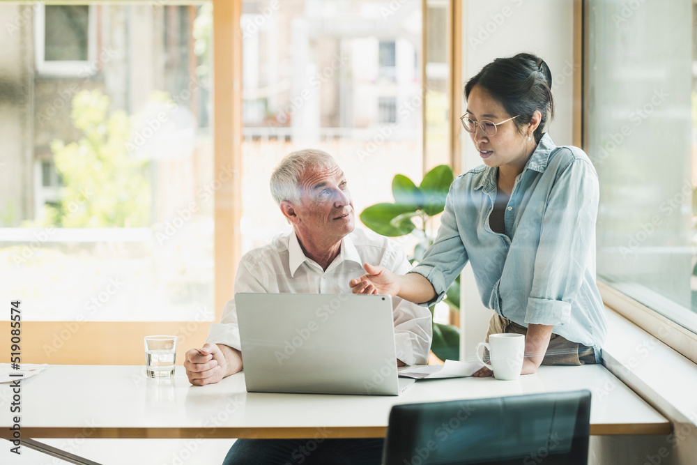 Businessman with colleague discussing over laptop in office Businessman with colleague discussing over laptop in office