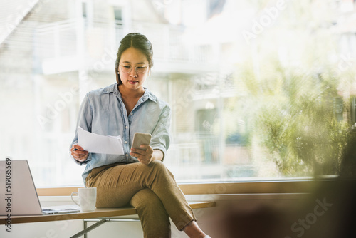 Businesswoman with document and smart phone at office