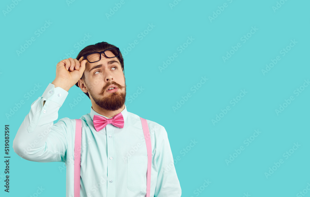 Surprised bearded Caucasian man looks up, raising glasses from eyes, carefully reads text or advertising offer dressed in white shirt and pink bow tie, stands on turquoise background in studio Surprised bearded Caucasian man looks up, raising glasses from eyes, carefully reads text or advertising offer dressed in white shirt and pink bow tie, stands on turquoise background in studio