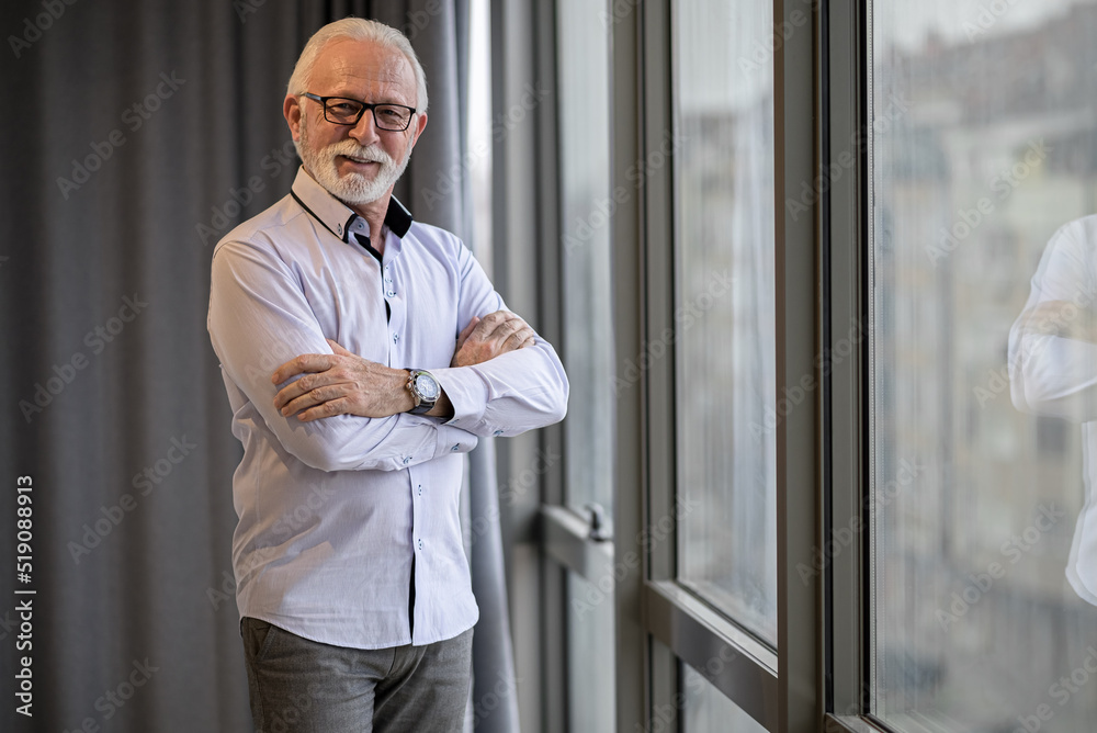 Portrait of confident senior entrepreneur standing by window at corporate office