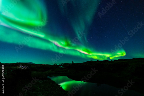 Northern lights with dark water canal and green reflections