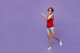 Full body young smiling happy fun woman 20s she wear red tank shirt eyeglasses walking goign strolling point index finger aside on workspace area isolated on plain purple backround studio portrait
