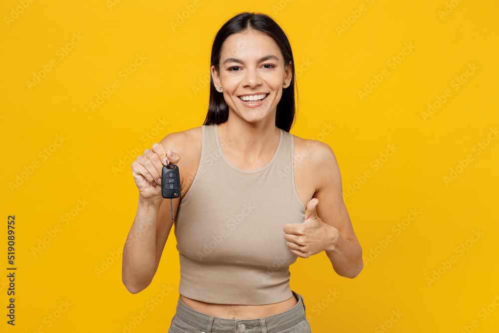 Young satisfied smiling happy cool latin woman 30s she wear basic beige tank shirt hold car key fob keyless system show thumb up gesture isolated on plain yellow backround. People lifestyle concept. Young satisfied smiling happy cool latin woman 30s she wear basic beige tank shirt hold car key fob keyless system show thumb up gesture isolated on plain yellow backround. People lifestyle concept.
