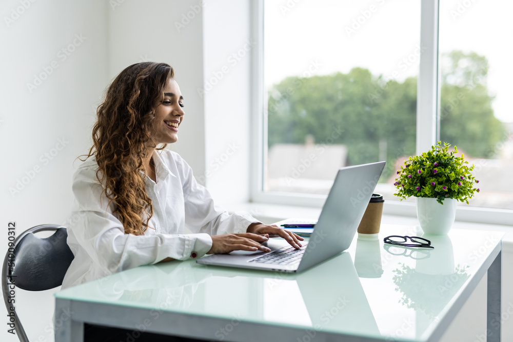 Fototapeta premium Young beautiful joyful woman smiling while working with laptop in office