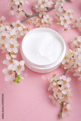 Container with bodycare and skincare cream on a pink background with blooming cherry. Cosmetic facial skin care and spa. Natural treatment concept.