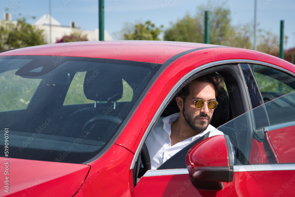 Handsome young man with beard, sunglasses and white shirt, inside his red sports car. Concept beauty, fashion, trend, luxury, motor, sports, winner. Handsome young man with beard, sunglasses and white shirt, inside his red sports car. Concept beauty, fashion, trend, luxury, motor, sports, winner.