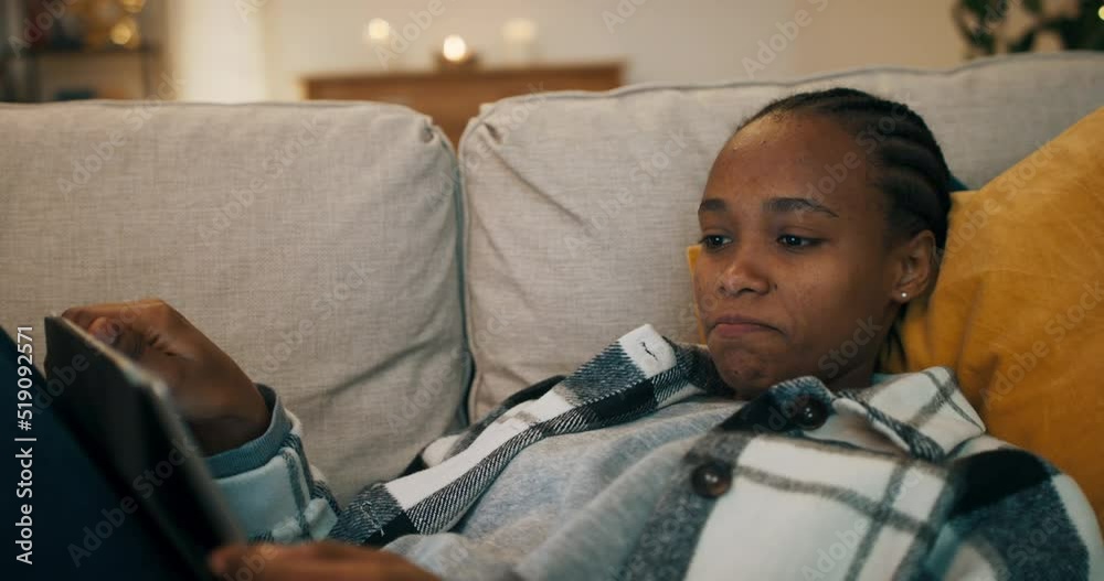 Attractive girl lying on couch in the living room, holding tablet and watching historical film. The girl worries about the heroes of the film, licks lips and enjoys watching. Attractive girl lying on couch in the living room, holding tablet and watching historical film. The girl worries about the heroes of the film, licks lips and enjoys watching.