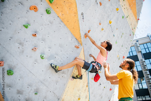 Male instructor insures a woman climbing an artificial wall of a climbing wall.