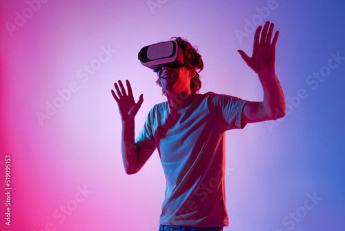 Amazed young man using a virtual reality headset playing video games trying to touch something with hand. © NaMong Productions