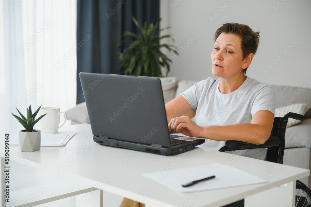 Positive elderly woman in wheelchair working on laptop, IT freelancer, online Positive elderly woman in wheelchair working on laptop, IT freelancer, online