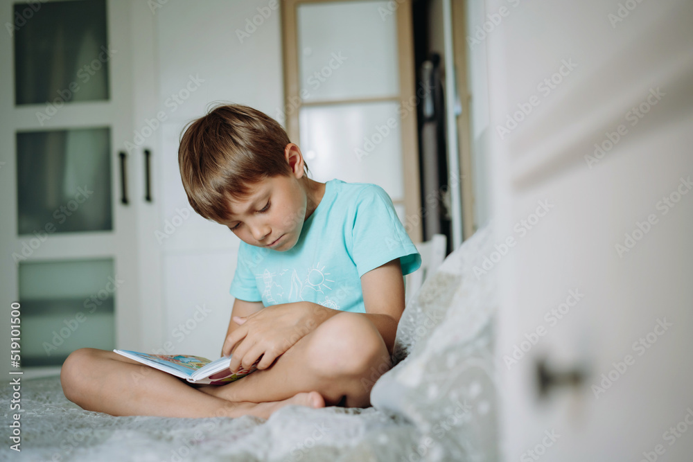 Cute caucasian boy reading a book sitting on bed in parents bedroom Cute caucasian boy reading a book sitting on bed in parents bedroom