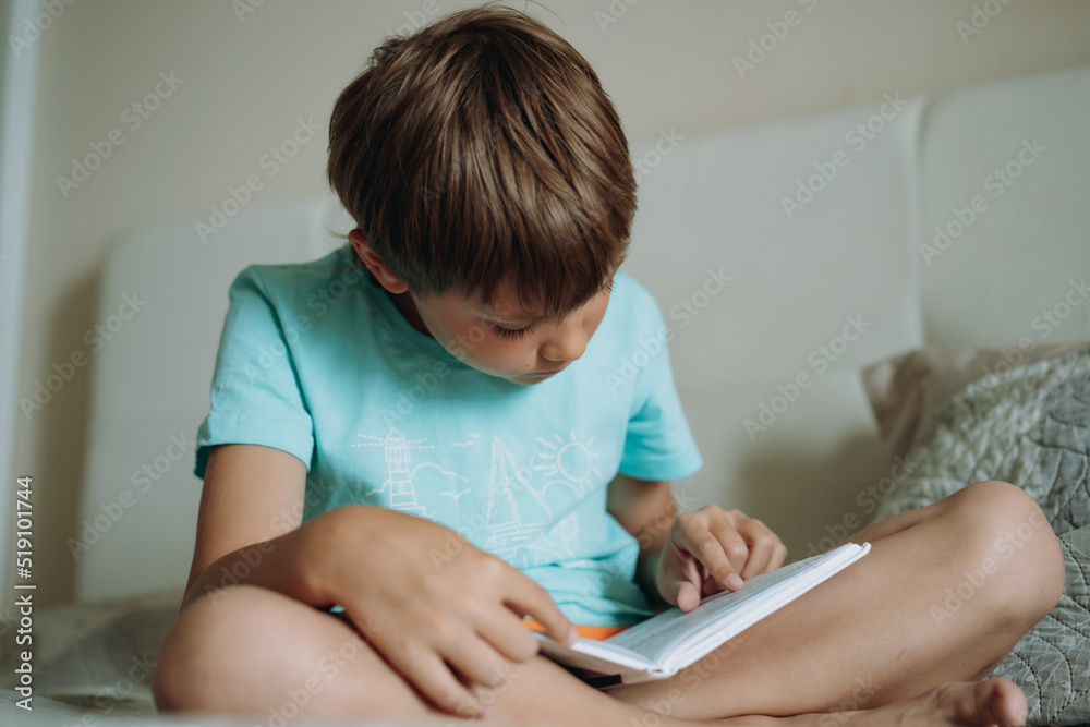 Cute caucasian boy reading a book sitting on bed in parents bedroom Cute caucasian boy reading a book sitting on bed in parents bedroom