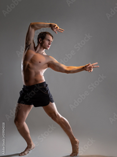 Muscular man in an artistic pose, portrait on a gray background. An athlete guy with spectacular muscles poses like an antique hero
