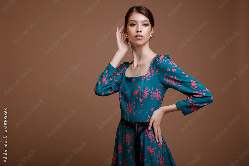 Fashion photo of a beautiful elegant young asian woman in a pretty blue ocean color dress with a floral pattern posing over brown coffee background. Studio Shot. Portrait